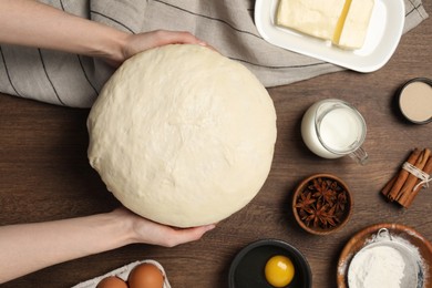 Woman holding fresh dough at wooden table, top view. Cooking yeast cake