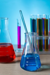 Photo of Different laboratory glassware with colorful liquids on wooden table against light blue background