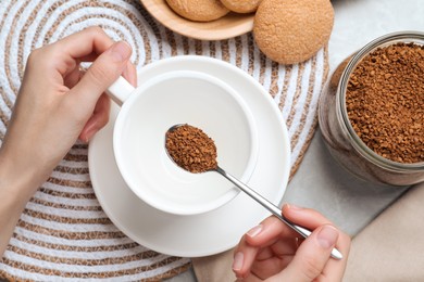 Photo of Woman pouring instant coffee into cup at light grey marble table, top view