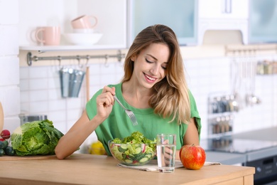 Woman eating vegetable salad at table in kitchen. Healthy diet