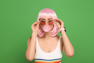 Photo of Beautiful woman in sunglasses blowing bubble gum on green background