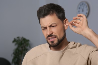 Photo of Emotional man cleaning ears and suffering from pain in room