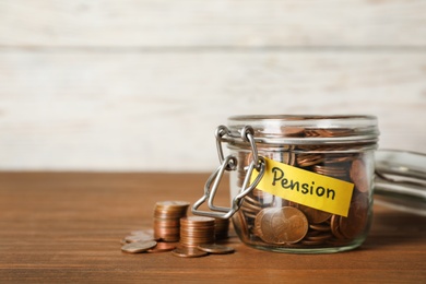 Coins in glass jar with label "PENSION" on table against light wall. Space for text