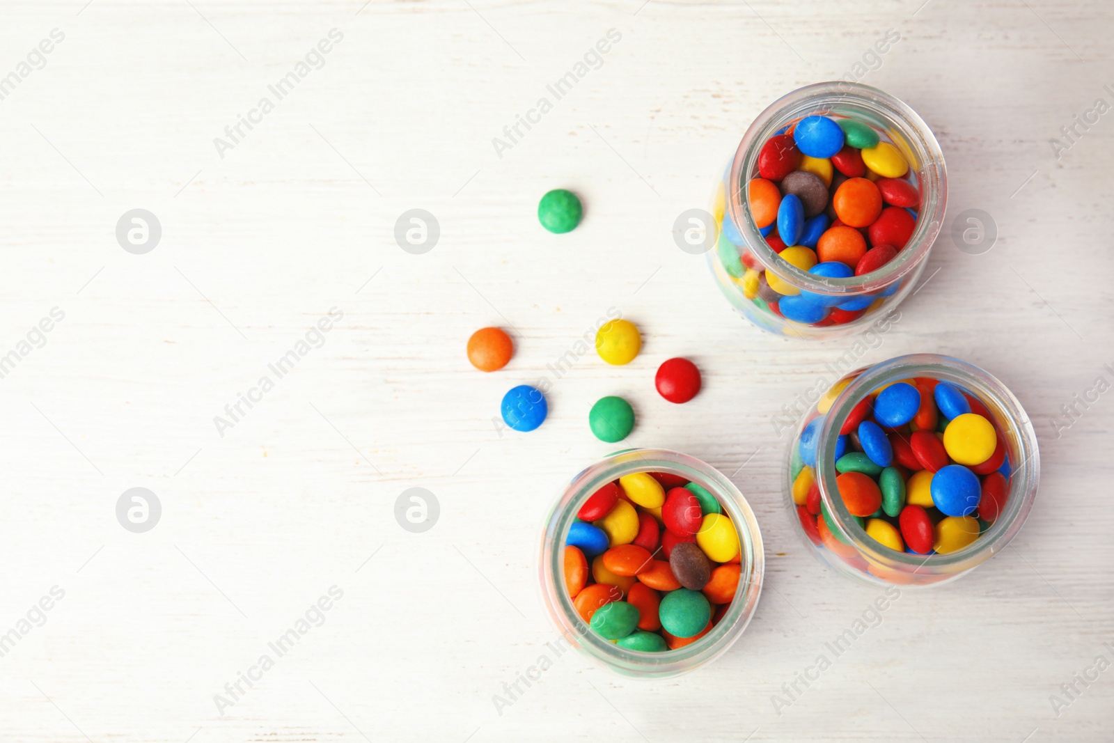 Photo of Jars with colorful candies on white wooden background, top view. Space for text