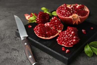 Photo of Cut fresh pomegranate, green leaves and knife on grey table
