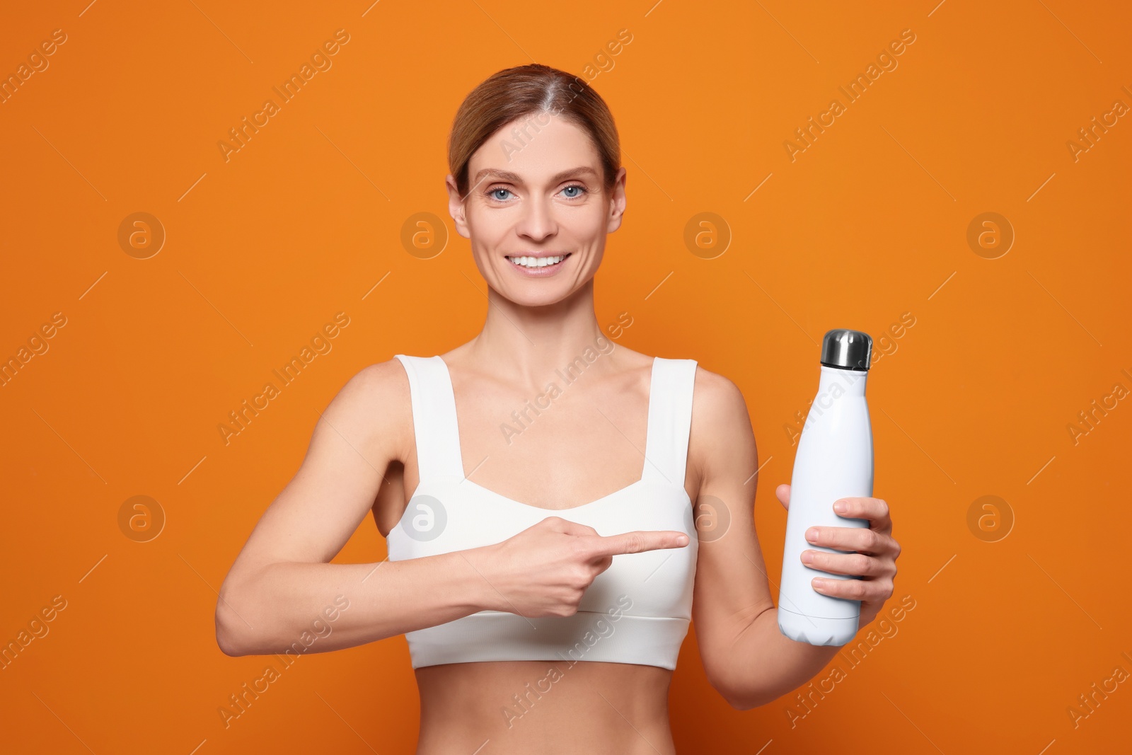 Photo of Sportswoman with thermo bottle on orange background