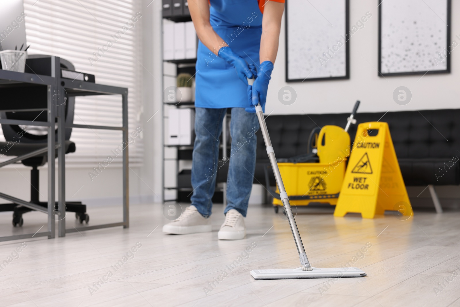 Photo of Cleaning service worker washing floor with mop, closeup. Bucket with wet floor sign in office