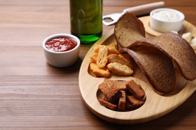 Photo of Tray with different crispy rusks, beer and dip sauces on wooden table
