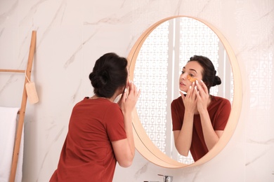 Photo of Young woman with eye patches near mirror in bathroom