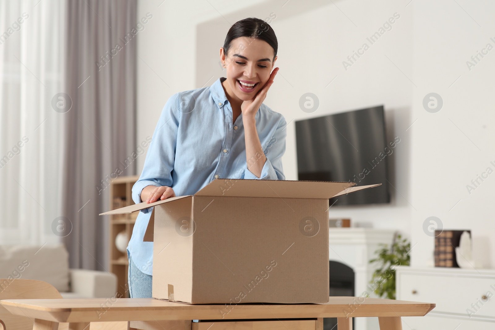 Photo of Emotional young woman with opened parcel at home. Internet shopping