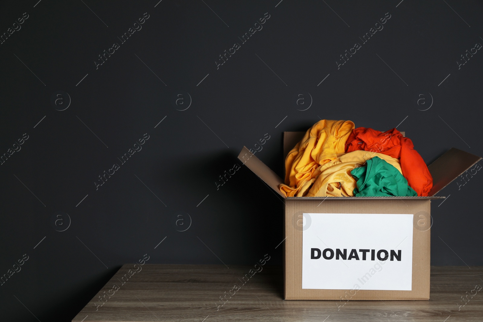 Photo of Donation box with clothes on table against black background. Space for text