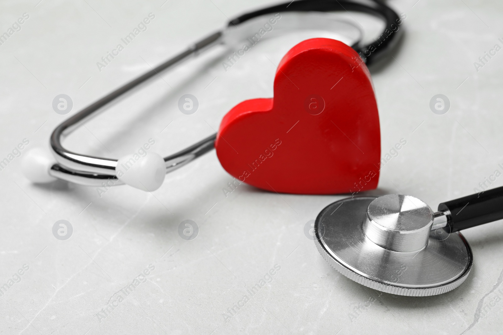 Photo of Stethoscope with red heart on light background, closeup