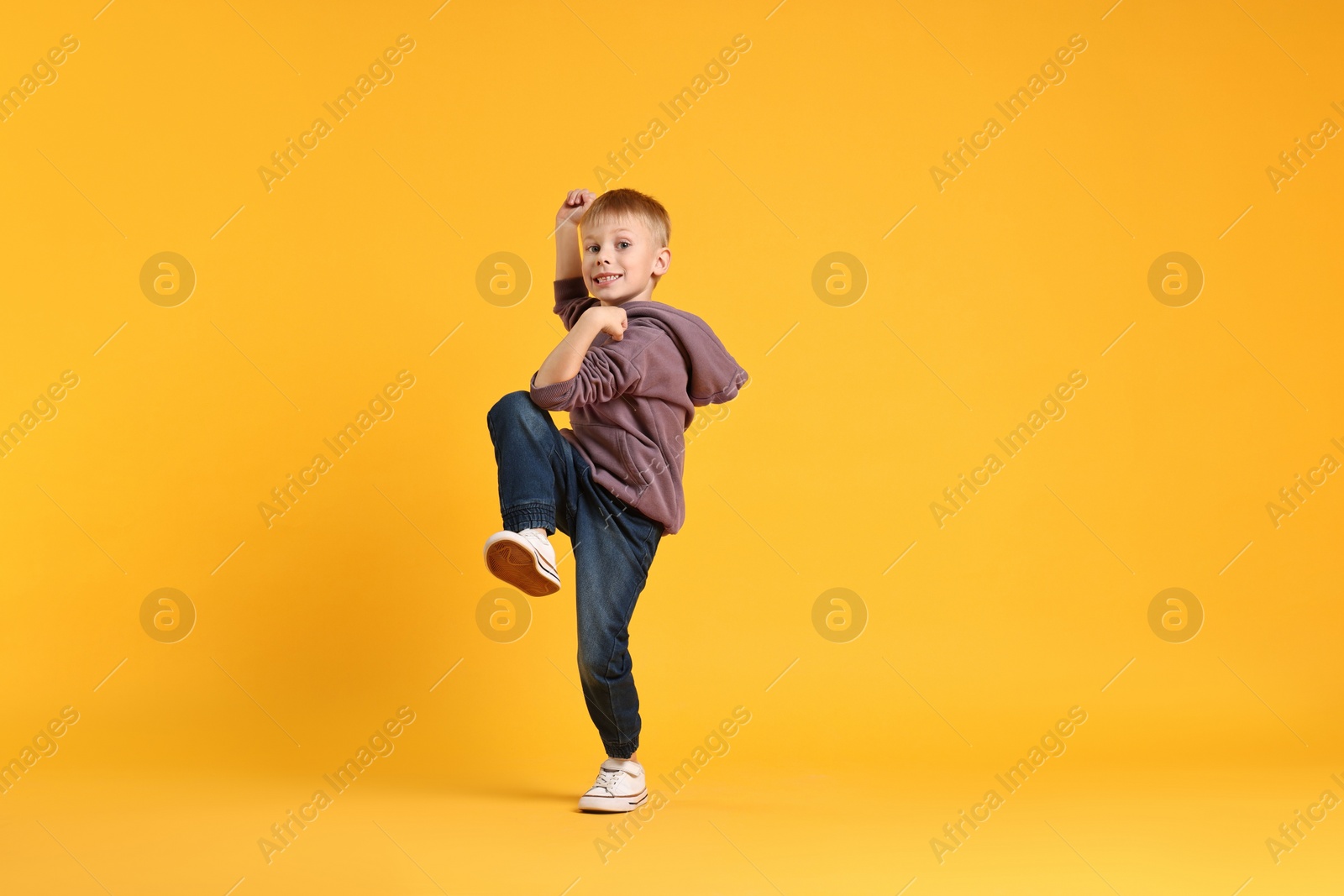 Photo of Happy little boy dancing on yellow background. Space for text