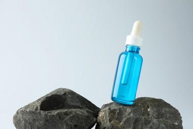 Photo of Bottle of cosmetic serum on stone against light grey background