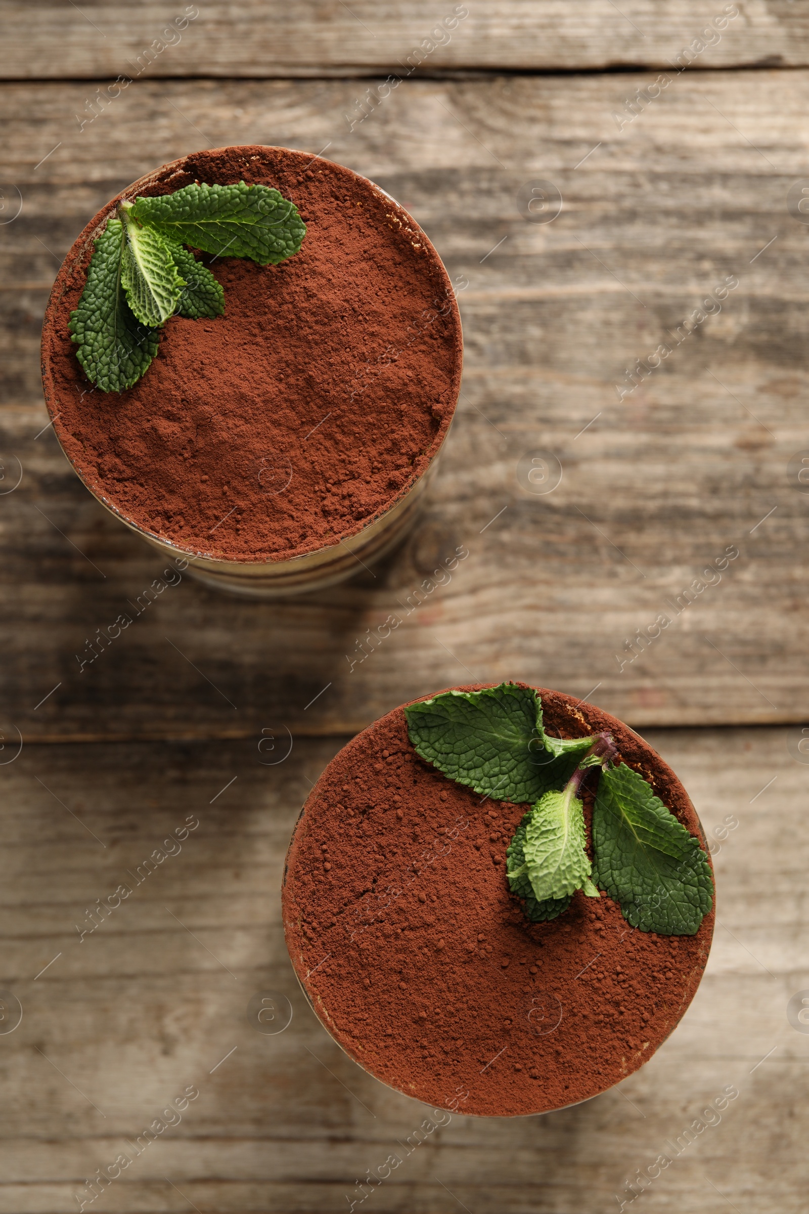 Photo of Tasty tiramisu and mint in glasses on wooden table, top view