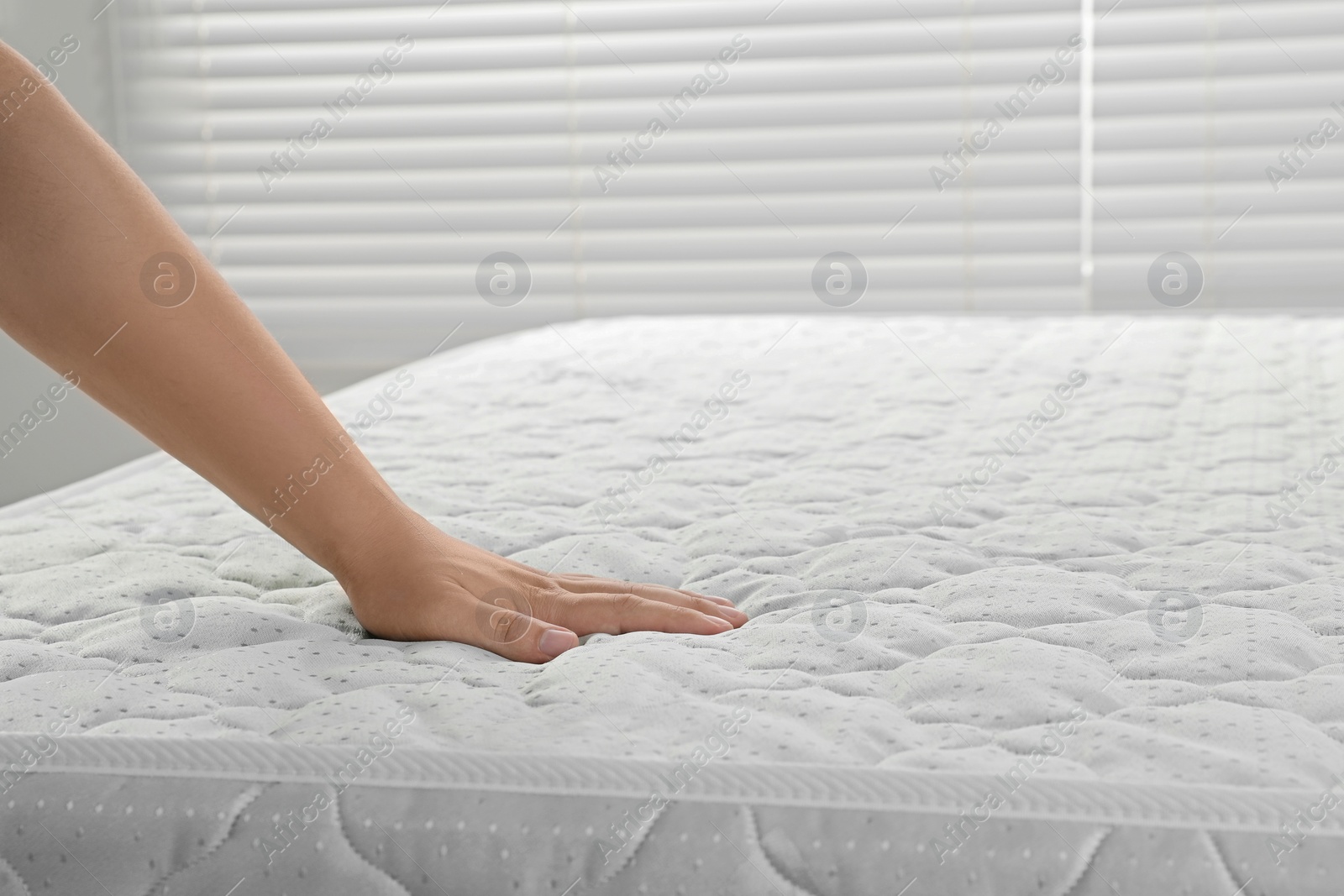 Photo of Woman touching soft light green mattress indoors, closeup