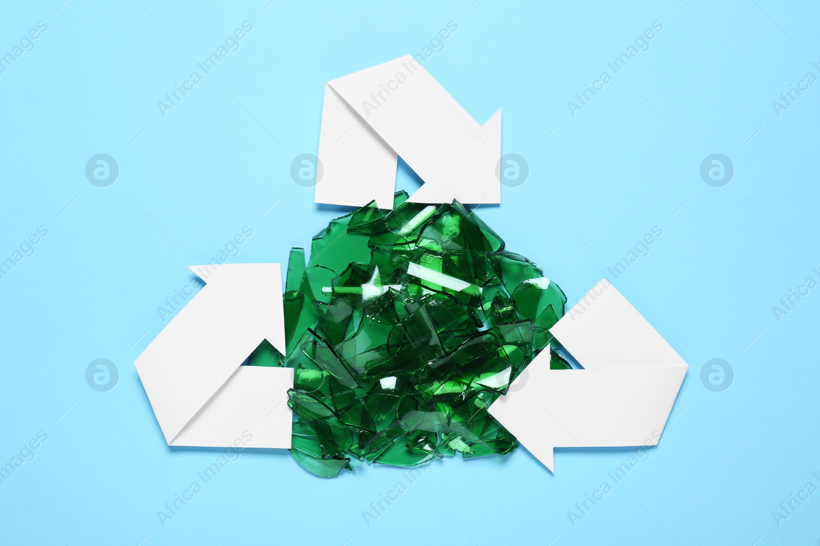 Photo of Recycling symbol and glass pieces on light blue background, flat lay