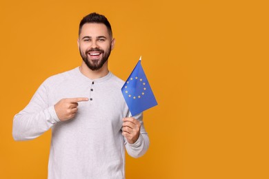 Photo of Young man holding flag of European Union on orange background, space for text