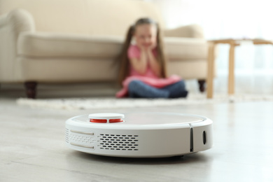 Photo of Little girl using robotic vacuum cleaner at home