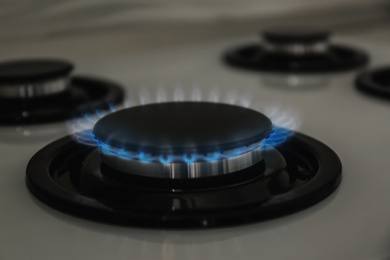Photo of Gas burner with blue flame on modern stove, closeup