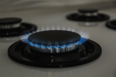 Gas burner with blue flame on modern stove, closeup