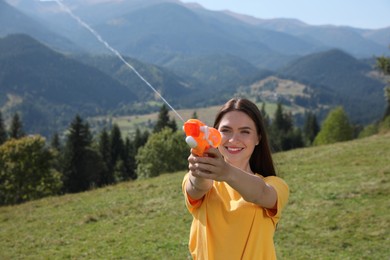 Happy woman with water gun having fun in mountains on sunny day