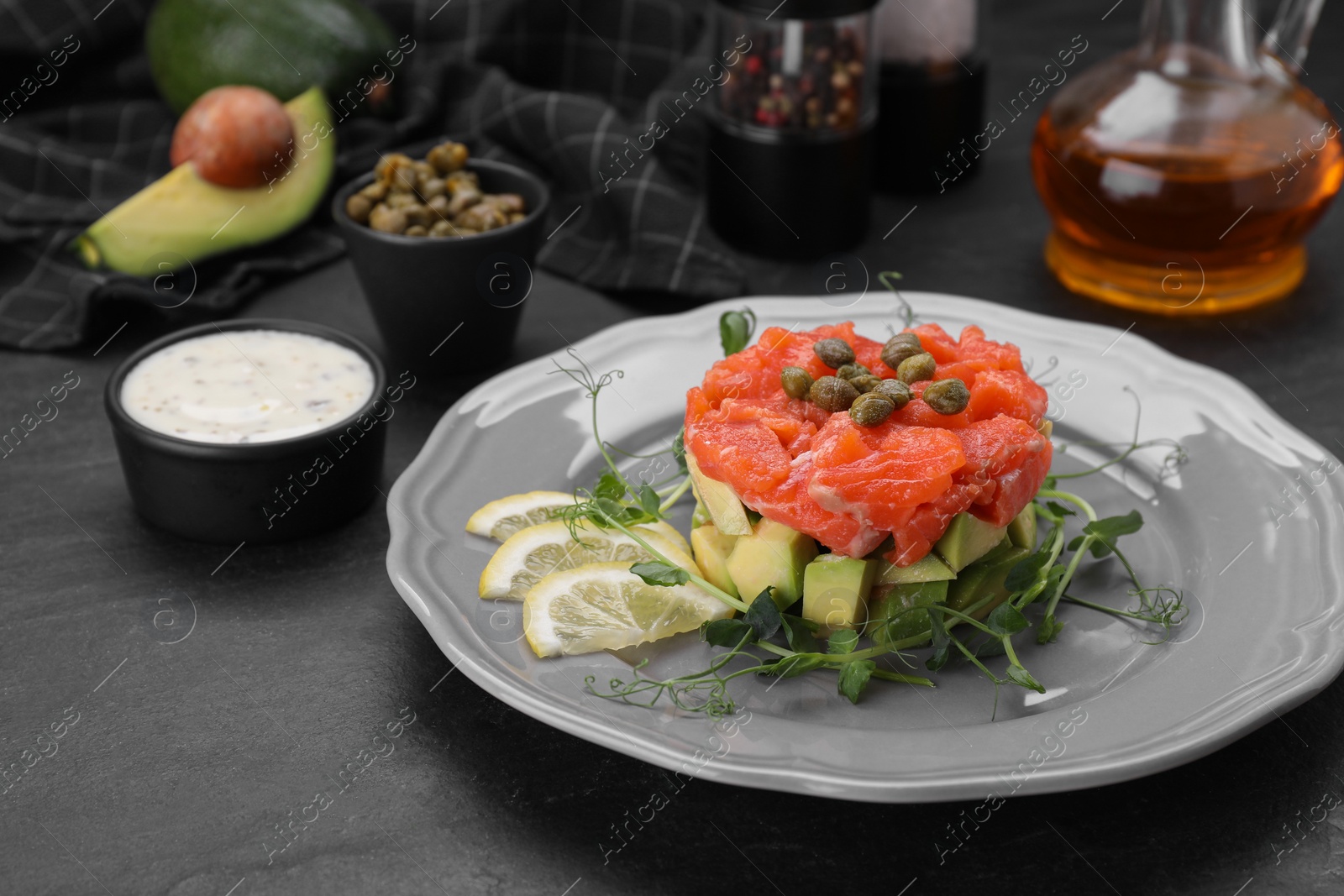 Photo of Delicious salmon tartare served with avocado and lemon on dark table