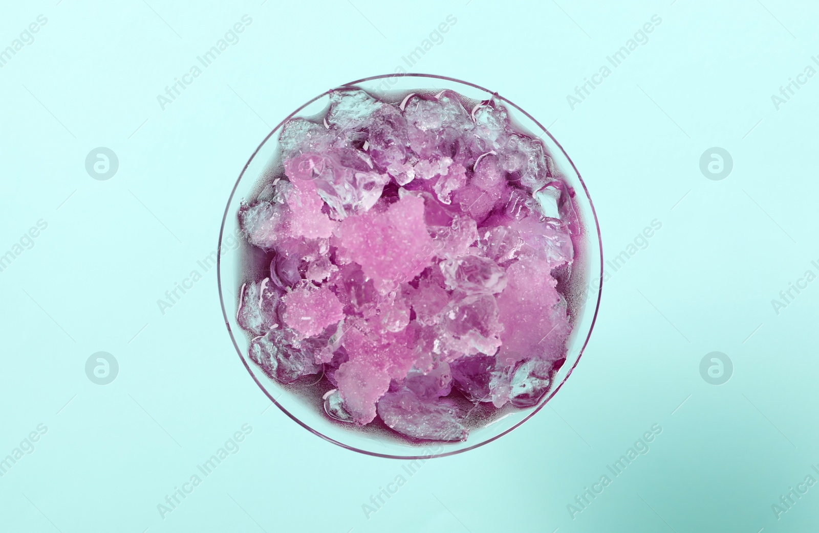 Photo of Shaving ice in martini glass on light blue background, top view