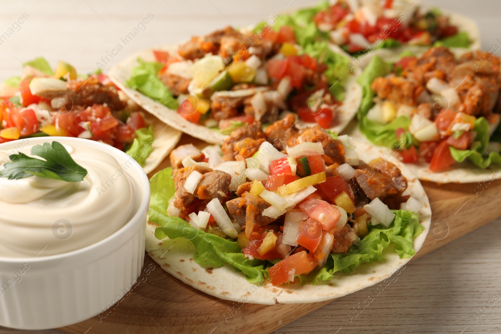 Photo of Delicious tacos with vegetables, meat and sauce on white wooden table, closeup