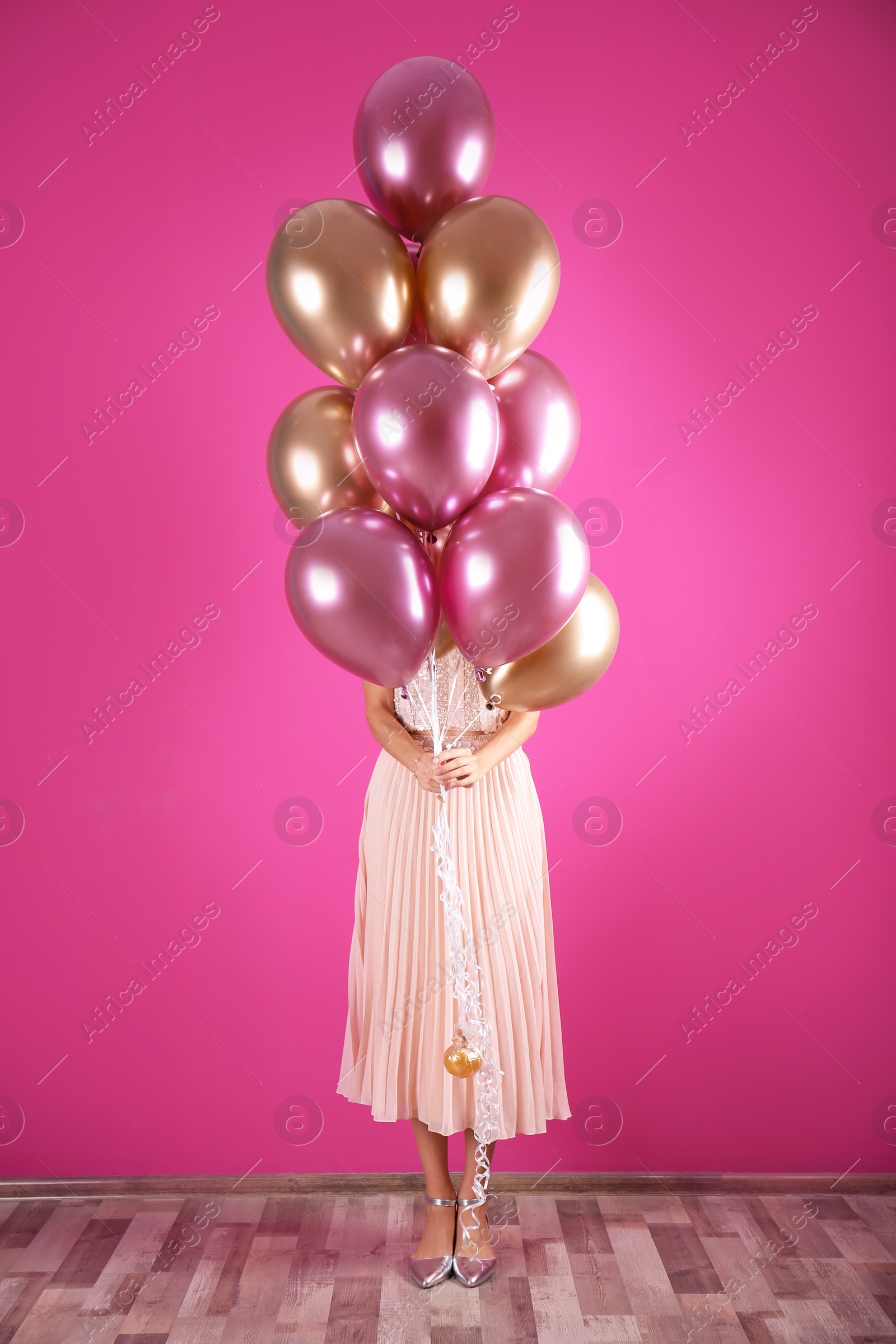 Photo of Young woman hiding behind air balloons near color wall