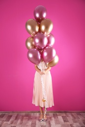 Young woman hiding behind air balloons near color wall