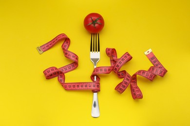 Fork, measuring tape and tomato on yellow background, flat lay. Diet concept