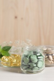 Jars with different pills on white wooden table, space for text. Dietary supplements