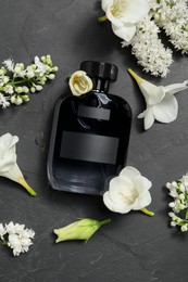 Photo of Bottle of luxury perfume and floral decor on black table, flat lay