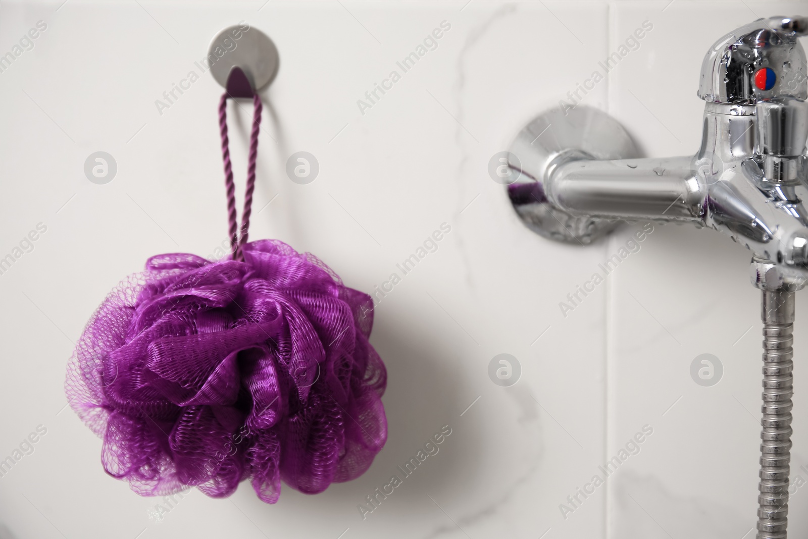 Photo of Purple shower puff hanging near faucet in bathroom