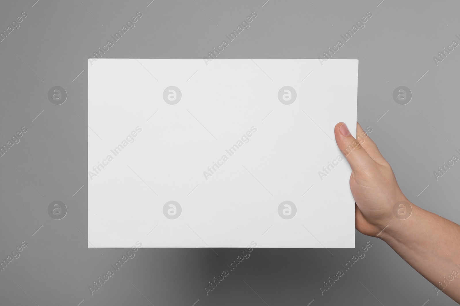 Photo of Woman holding sheet of paper on grey background, closeup. Mockup for design