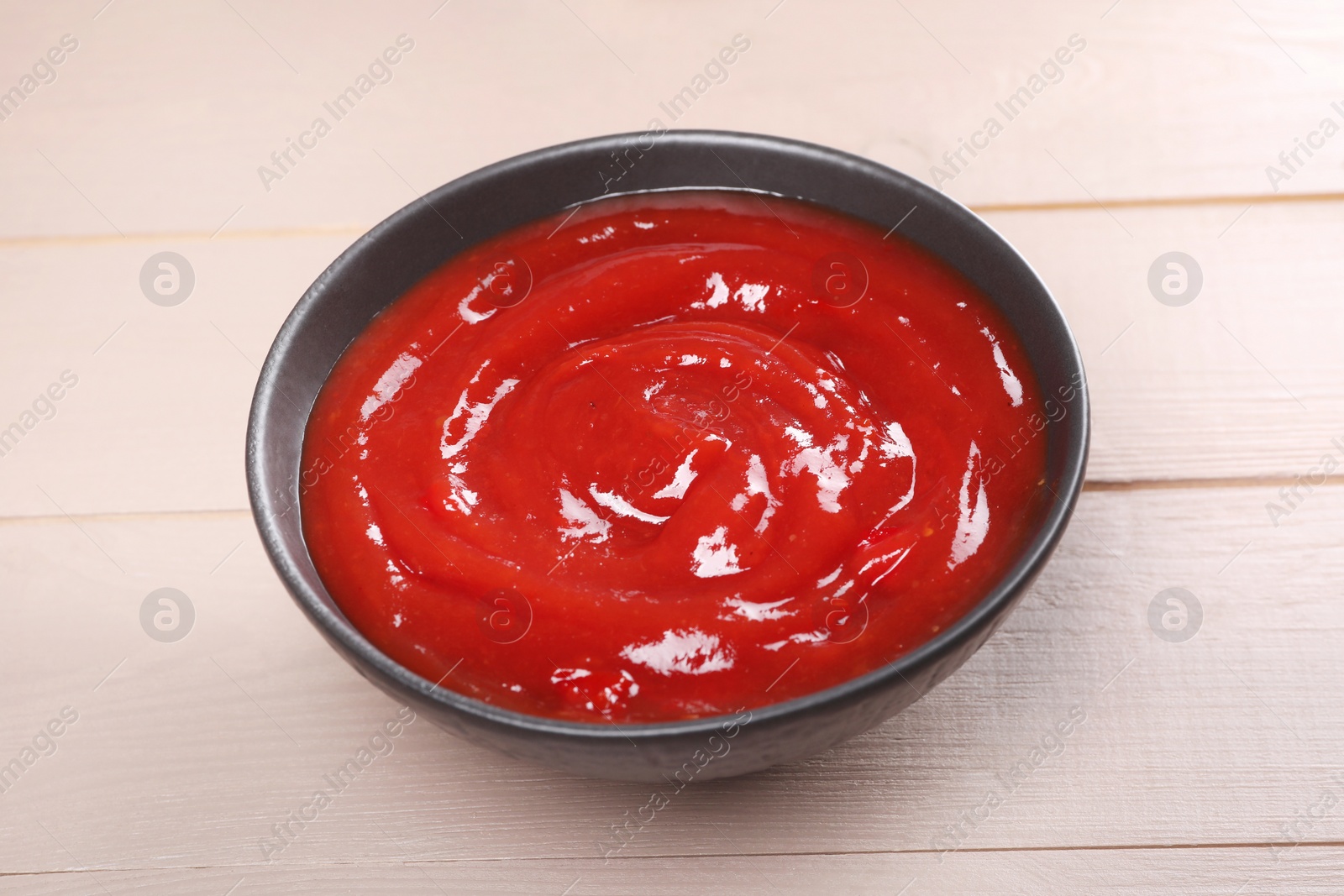 Photo of Delicious ketchup in bowl on light wooden table, closeup. Tomato sauce