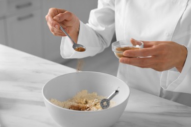 Photo of Professional chef adding cocoa powder into dough at white marble table indoors, closeup