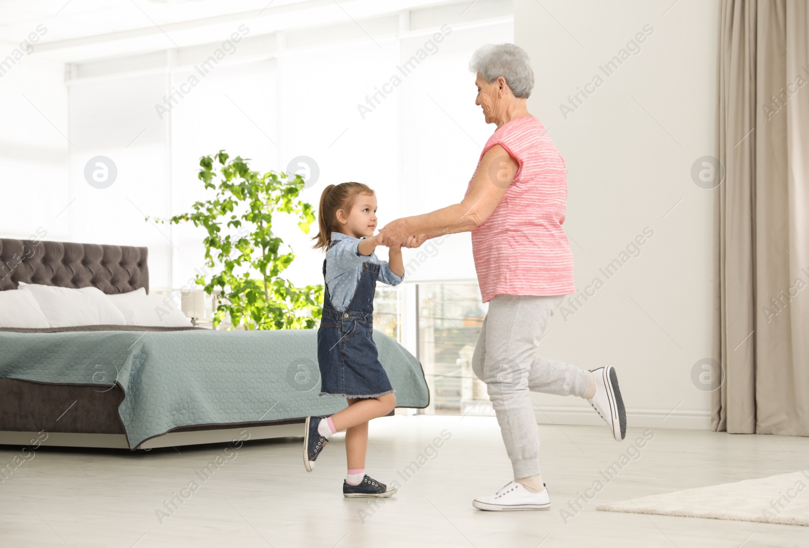 Photo of Cute girl and her grandmother dancing at home