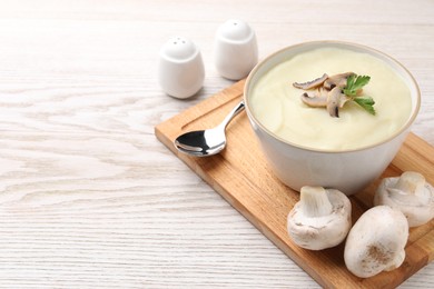 Photo of Bowl of tasty cream soup with mushrooms, parsley and spoon on light wooden table. Space for text