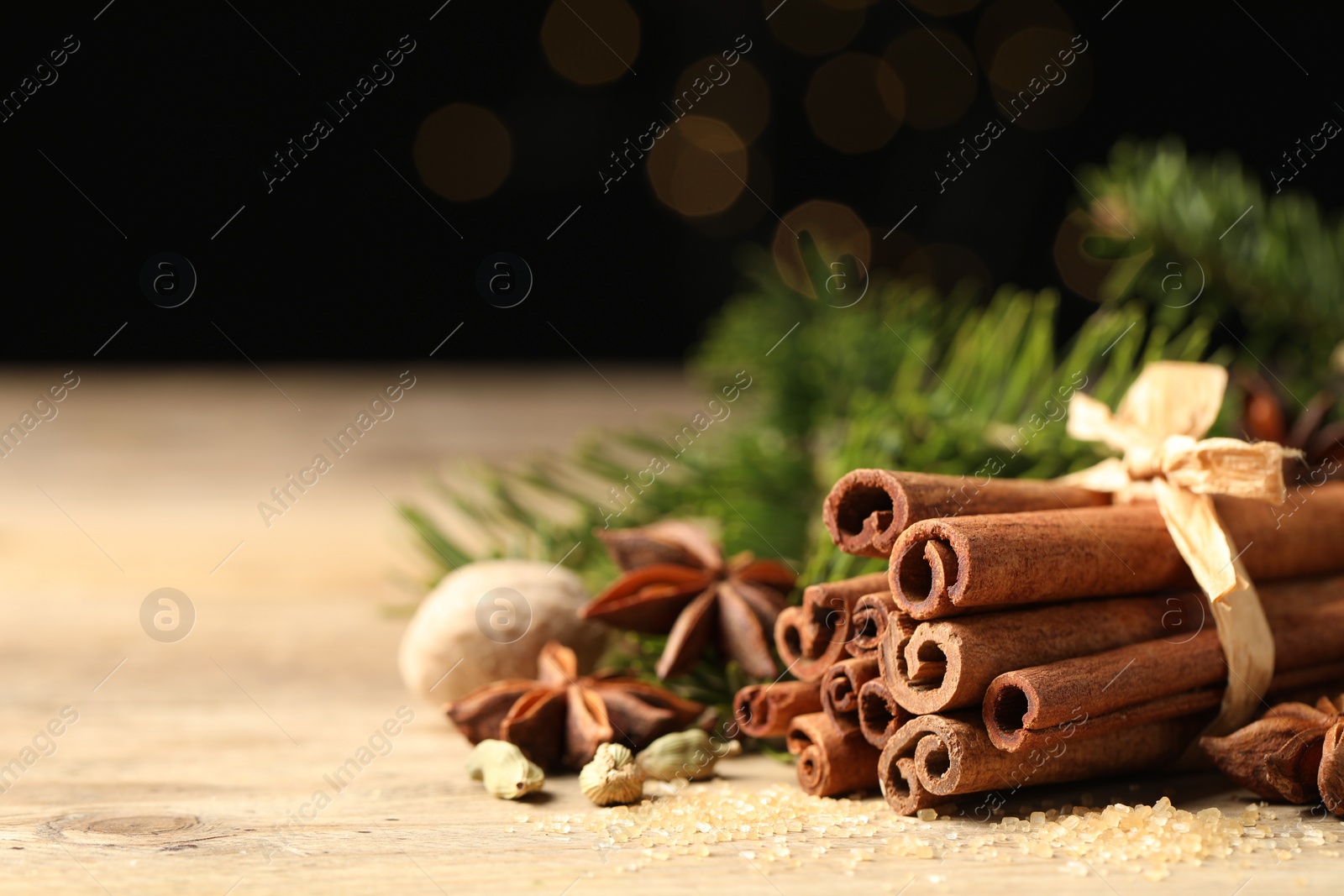 Photo of Different aromatic spices on wooden table against black background, closeup. Space for text