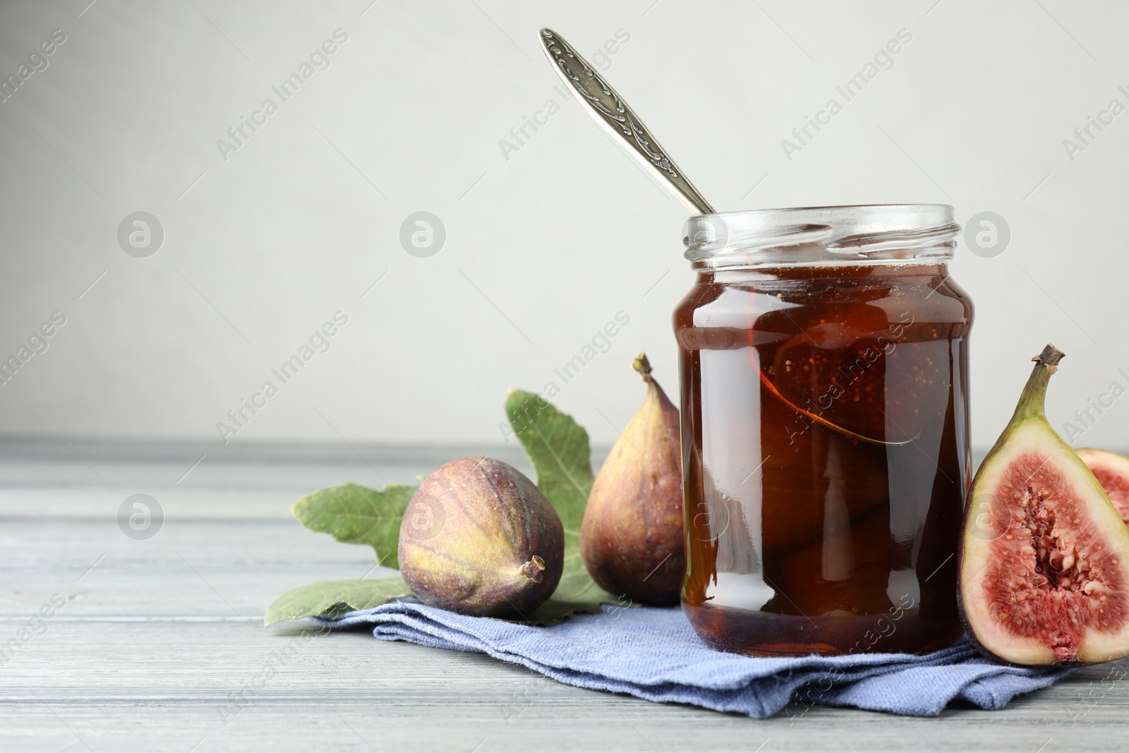 Photo of Jar of tasty sweet jam and fresh figs on grey table, space for text