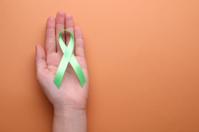 Photo of World Mental Health Day. Woman holding green ribbon on pale orange background, top view with space for text