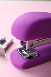 Photo of Bright stapler with staples on pink background, closeup