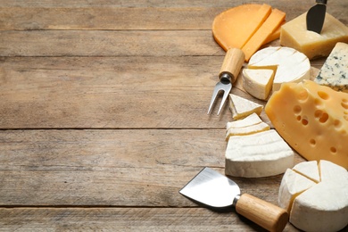 Photo of Set of different cheeses and specialized knives and fork on wooden table. Space for text