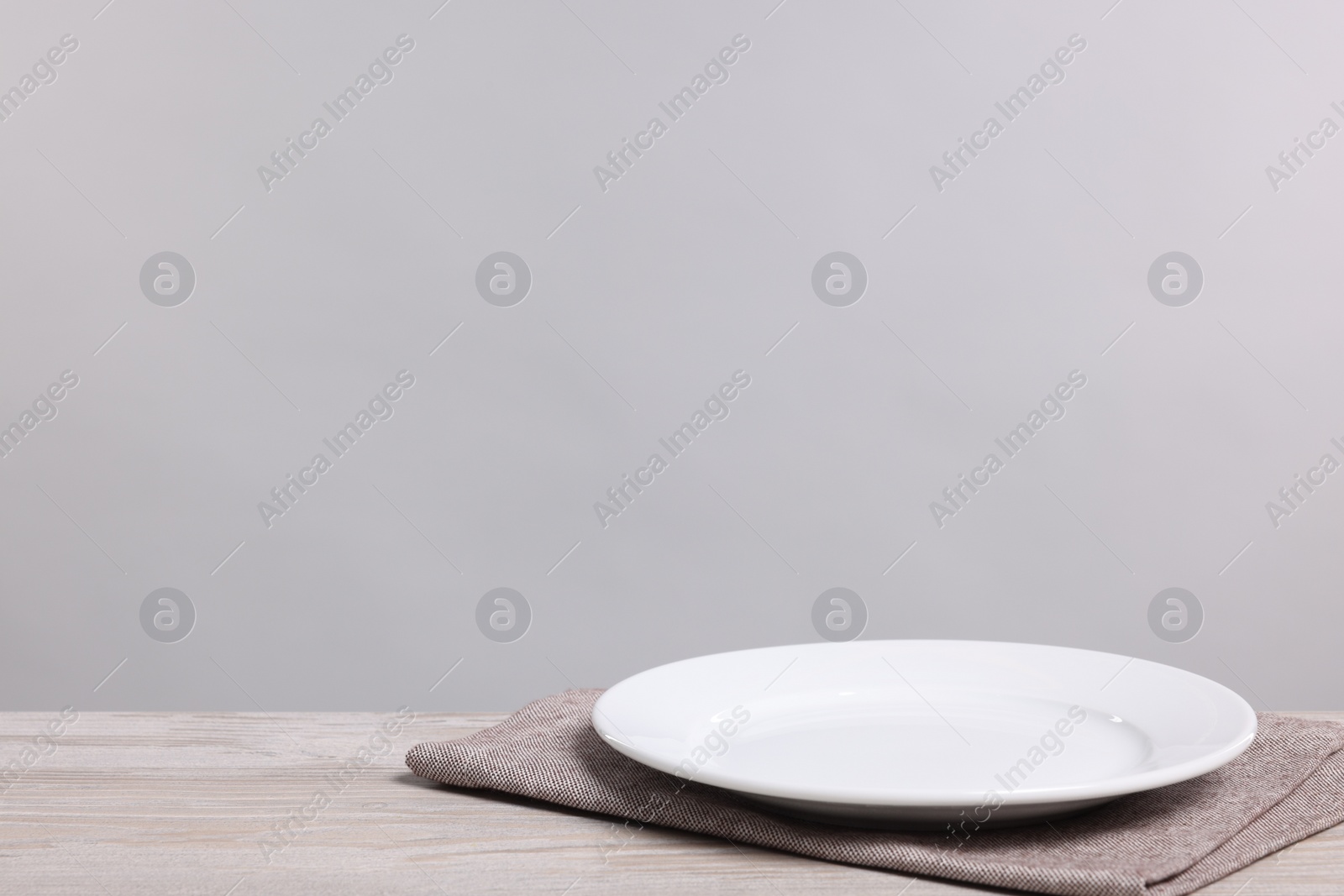 Photo of Empty ceramic plate on wooden table against light background, space for text