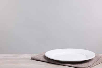 Photo of Empty ceramic plate on wooden table against light background, space for text