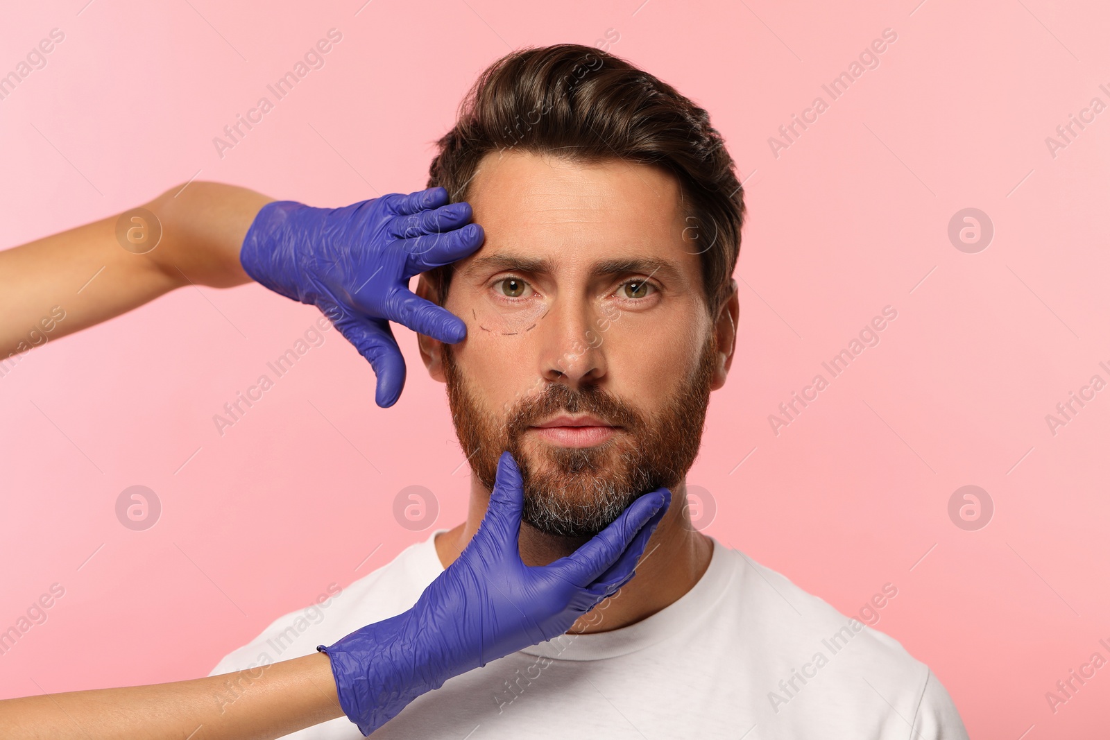 Photo of Doctor checking patient's face before cosmetic surgery operation on pink background