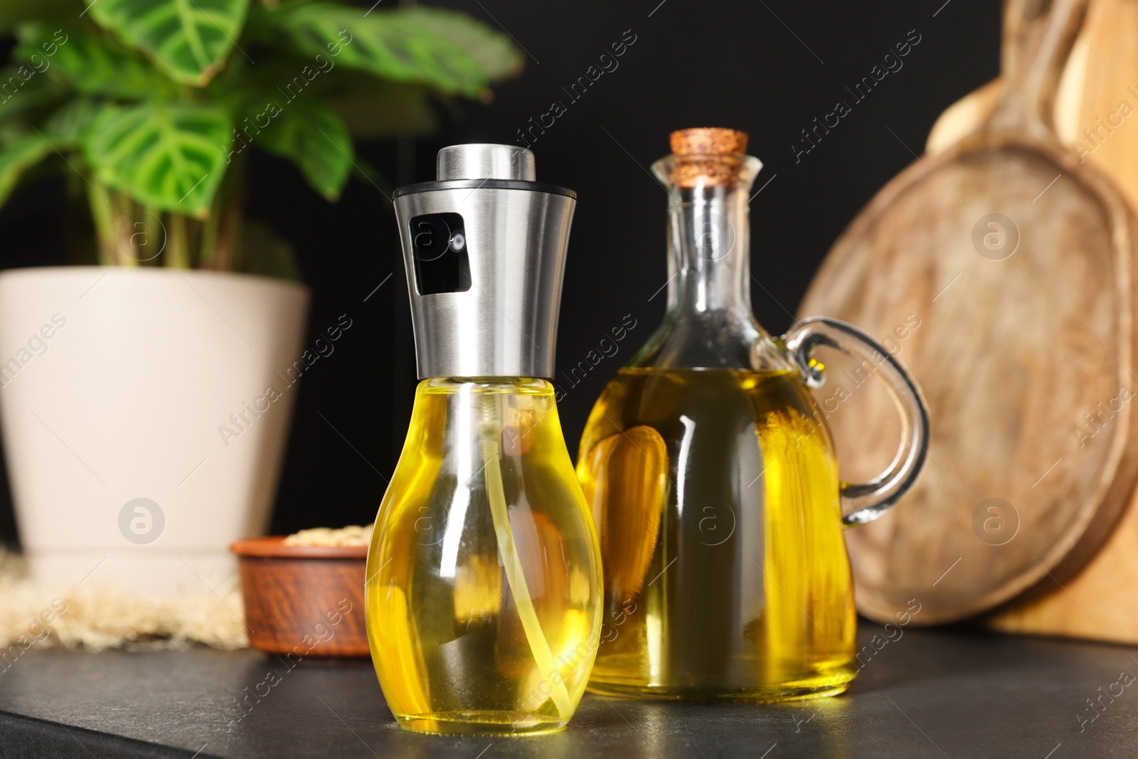 Photo of Bottles with cooking oil and bowl of sunflower seeds on black table in kitchen