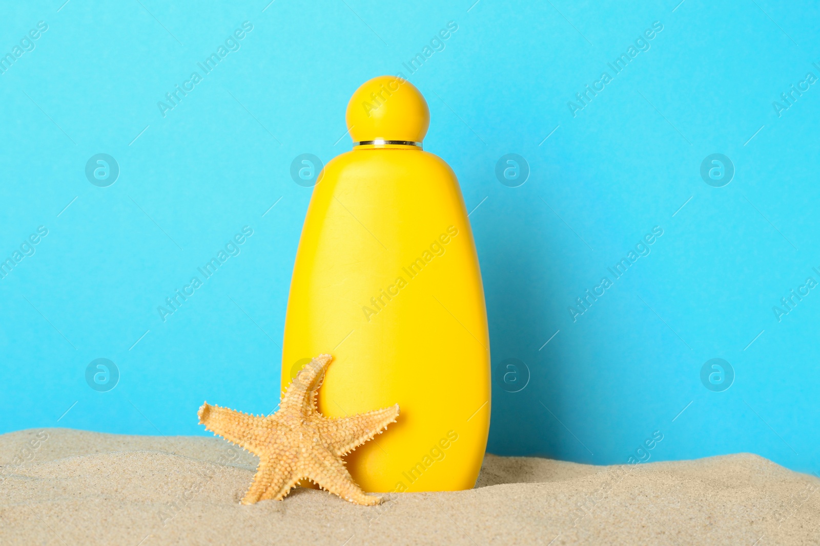 Photo of Suntan product and starfish on sand against light blue background